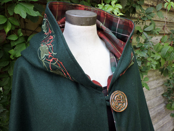 Green cloak with PEI tartan and embroidered details on a mannequin against a natural background