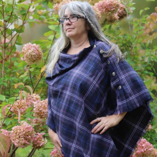 Person wearing a Scottish Heather Tartan cape in a garden setting with pink flowers.
